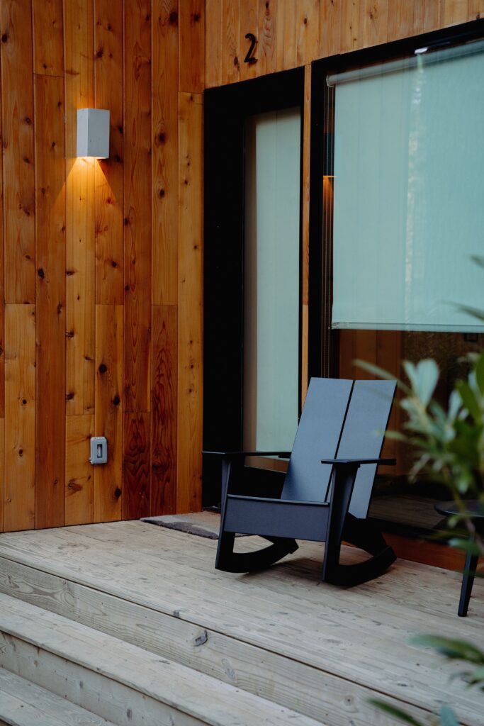 A vertical shot of a modern wooden porch with a black rocking chair and a wall light fixture
